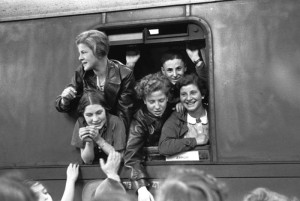 Five young persons waving out of a trainwindow
