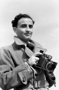 Black and white picture of an man with a camera in his hands. He looks directly at the phtographer