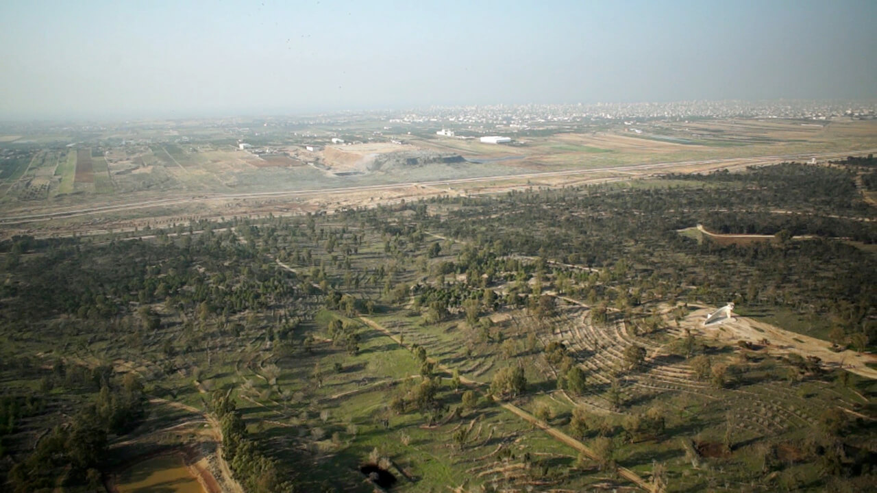 View of a green landscape. In the background of the picture you can see a densely populated region, behind it you can guess the sea.