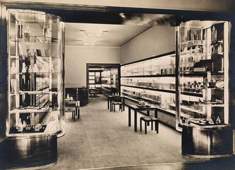 Black and white photograph of the interior view of a store with illuminated showcases.