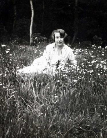  A woman is lying in a meadow in a white dress with a short haircut.