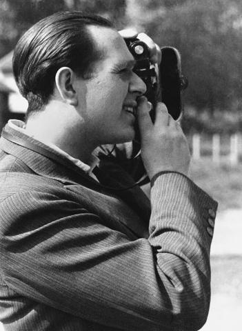 Die Aufnahme zeigt Fred Stein im Seitenprofil beim Fotografieren. Er trägt ein Nadelstreifen-Jackett und ein Hemd ohne Krawatte.