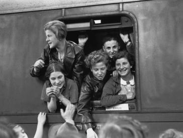 Black and white photography of teenage girls and boys joyfully leaning out of the window of a train