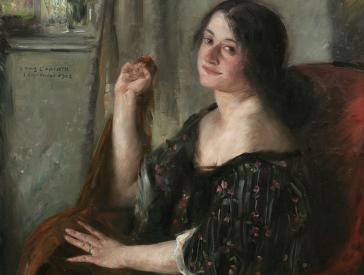 Portrait of a woman (Charlotte Berend) sitting in three-quarter profile on a red armchair in front of a window.