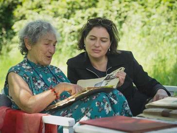 Zwei Frauen sitzen auf einer Garten Bank und blättern gemeinsam in einem Fotoalbum.