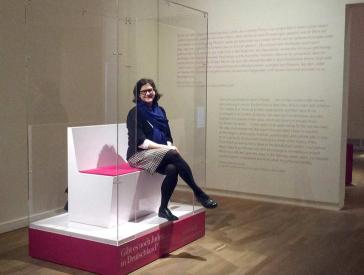 A woman sitting on a bench in a vitreous showcase open at the front.