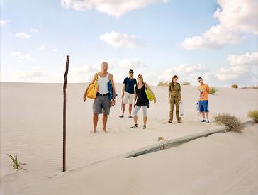 A middle-aged man and woman and two younger men and a younger woman on the beach. The young woman is in uniform, all the others are wearing summer clothes.