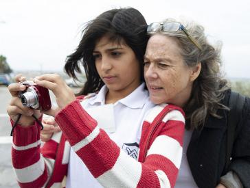 A girl has a digital camera in her hand, an older woman puts her head on her shoulder.