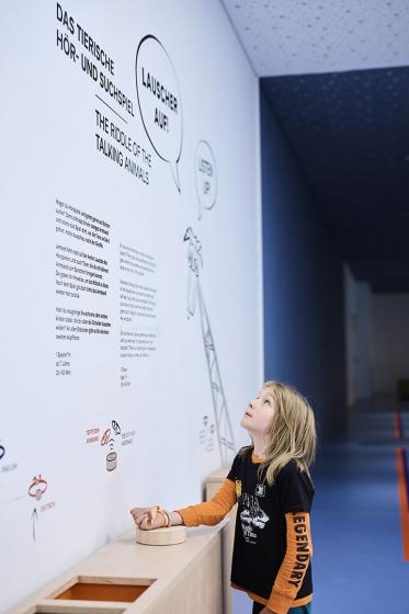 Child with blond hair looks at pictures and text on a wall.