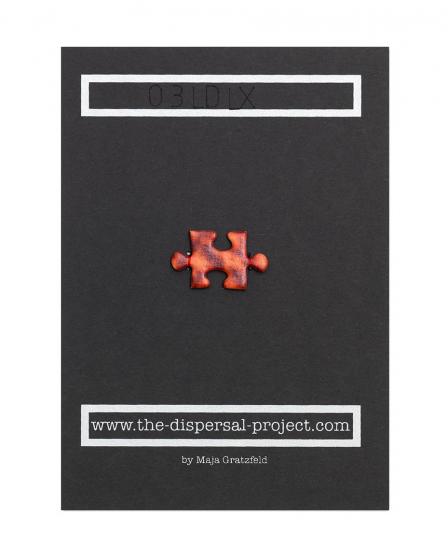 A picture-puzzle piece made of photo mounting board has been sewn with red thread onto the center of a piece of black cardboard