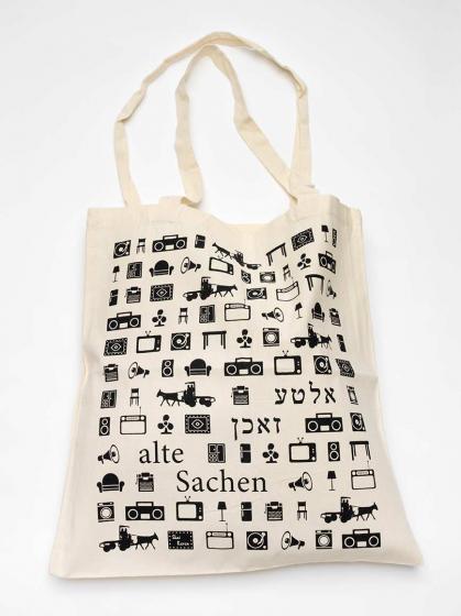 Canvas bag covered in pictograms of furniture, boom boxes, megaphones, horse-drawn carriages, and the label “alte Sachen,” meaning “old things,” in German and Yiddish