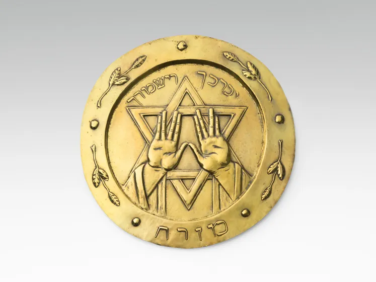 Goldfarbener Teller mit hebräischer Schrift, Davidstern und zwei Händen.