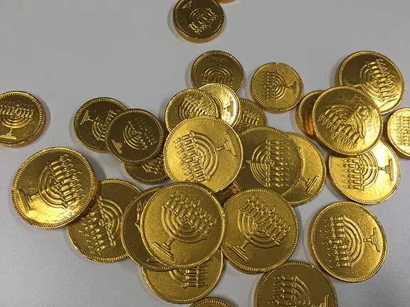 Taler aus Schokolade. Diese sind in goldglänzende Folie verpackt, in die Chanukka-Leuchter eingeprägt sind.