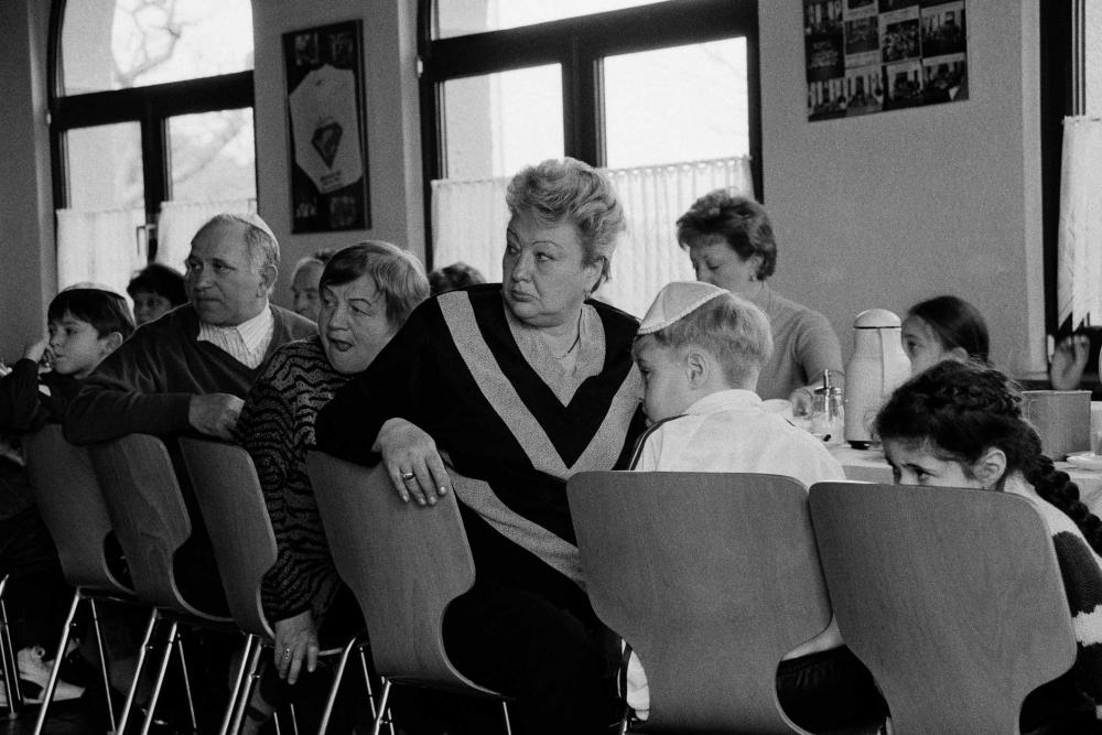 Black and white photograph of a group of people sitting at a table turning around in their seats to looks at something behind them, the men in the photo are wearing Yamakas