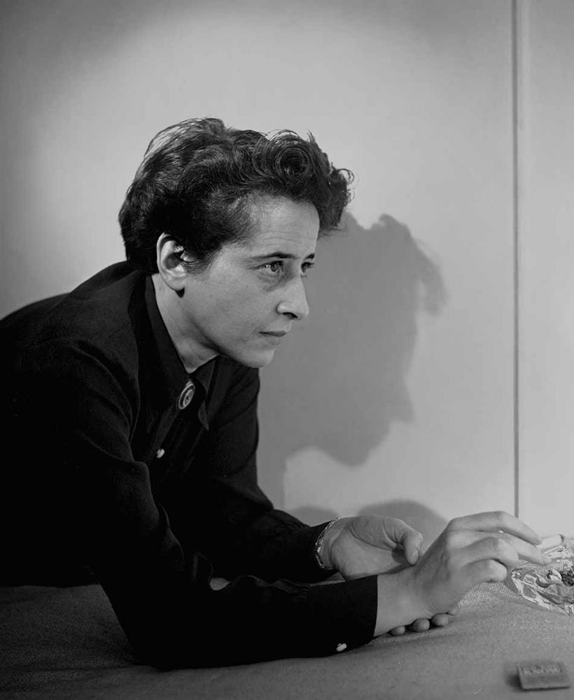 Black and white portrait of Hannah Arendt wearing a dark collar shirt leaning over an ashtray 