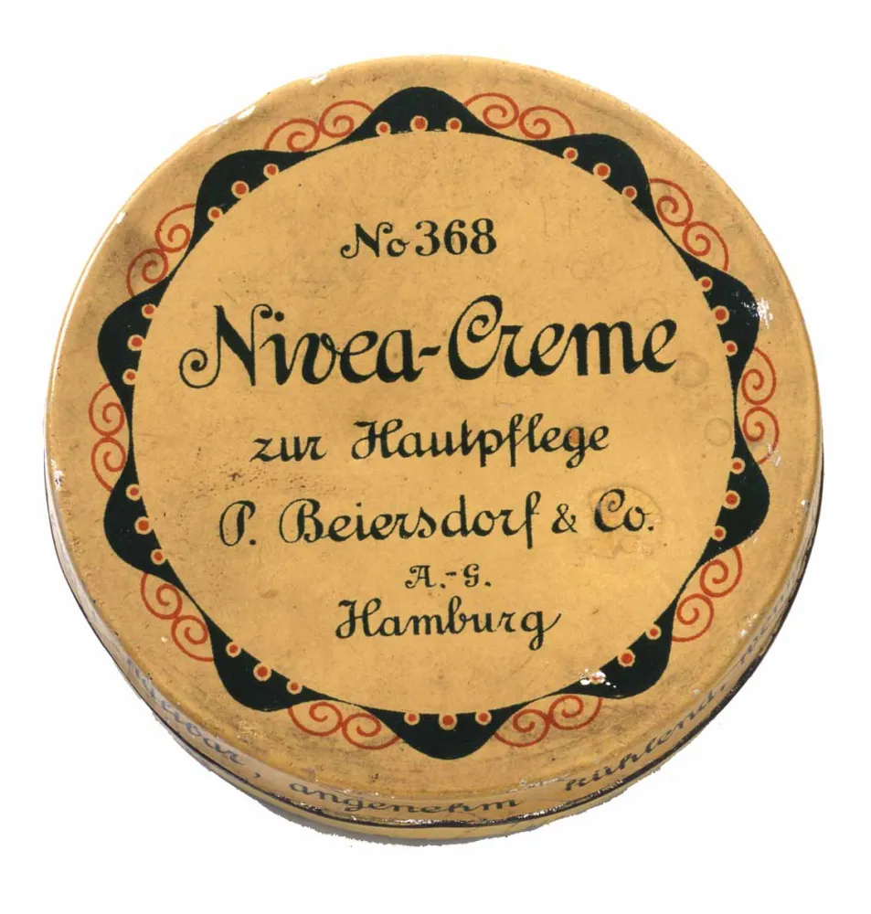 Kleine runde Dose, hellbeige mit grüner Beschriftung und rot-grünem Ornament als Umrandung. Beschriftung: „No. 368 Nivea-Creme zur Hautpflege P.Beiersdorf & Co A.-G. Hamburg.“