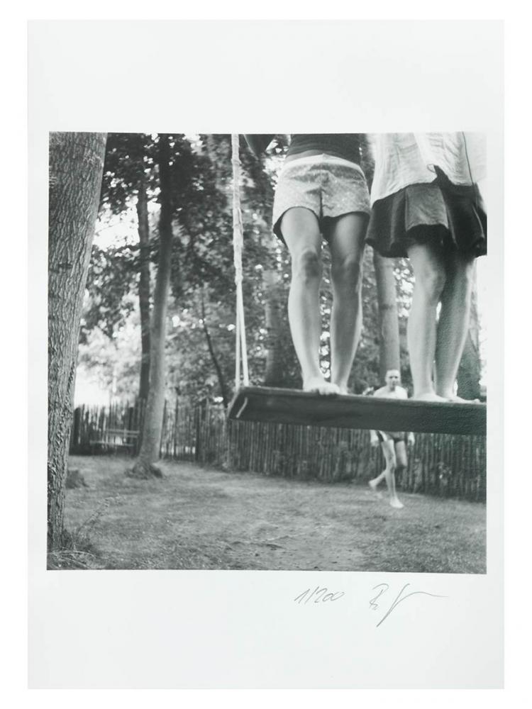 A black and white photo of two girls standing on a wide wooden swing. Only their legs are visible 