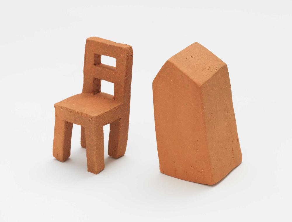 Miniatur-Tonskulpturen eines Stuhls und einer grabsteinförmigen Figur.