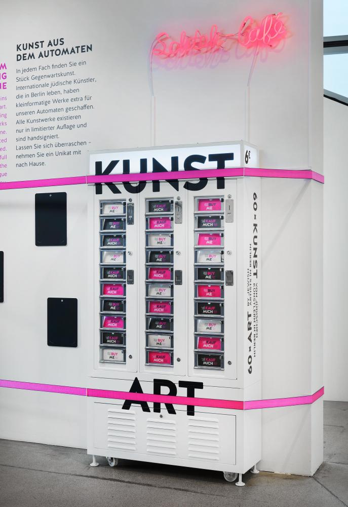 Ein großer weißer Automat mit dem Wort "ART" in fetten schwarzen Buchstaben, auf den kleinen Fächern des Automaten steht "Buy Me".
