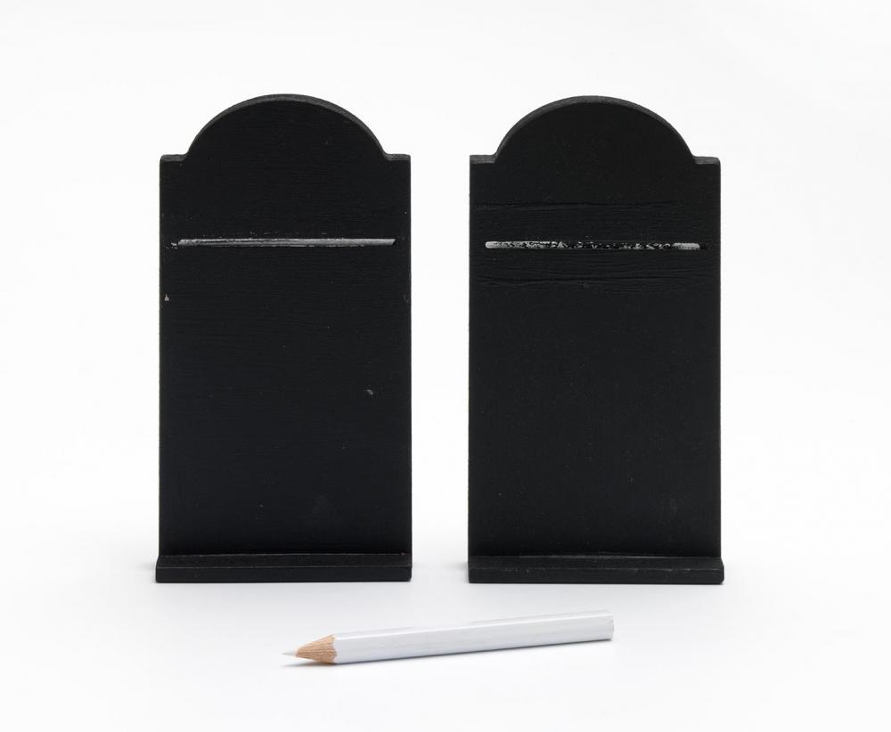 Zwei »Gebotstafeln« mit geschwungener Oberkante aus einer mitteldichten Holzfaserplatte mit schwarzer Tafelfarbe lackiert, davor liegt ein weißer Kreidestift
