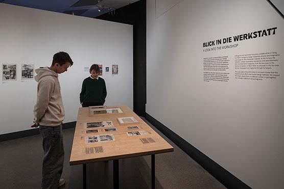 Raumansicht der Ausstellung "Het Onderwater Cabaret": zwei Besucher*innen schauen sich Objekte auf einem Tisch an.