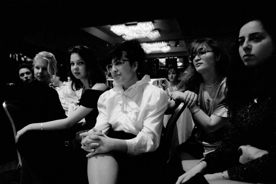 Black and white photograph of a group of nicely dressed women sitting in a large room with their hands in their lap, they are focused on something in the distance