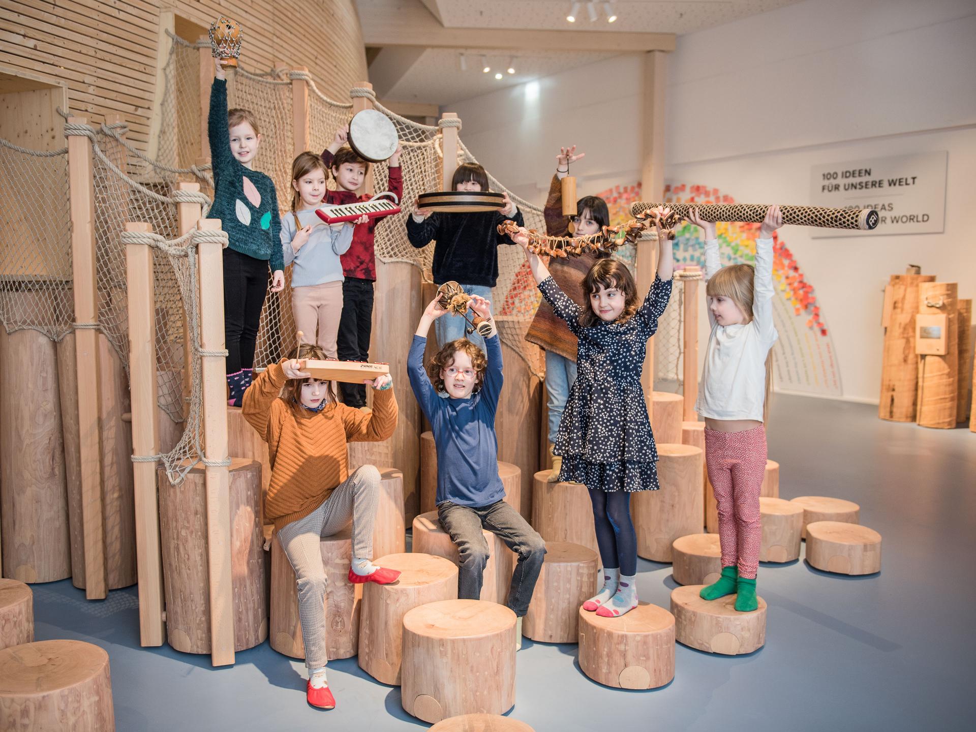 Neun Kinder stehen im Klanglabor om Kindermuseum ANOHA des Jüdischen Museums und halten Gegenstände in der Hand.
