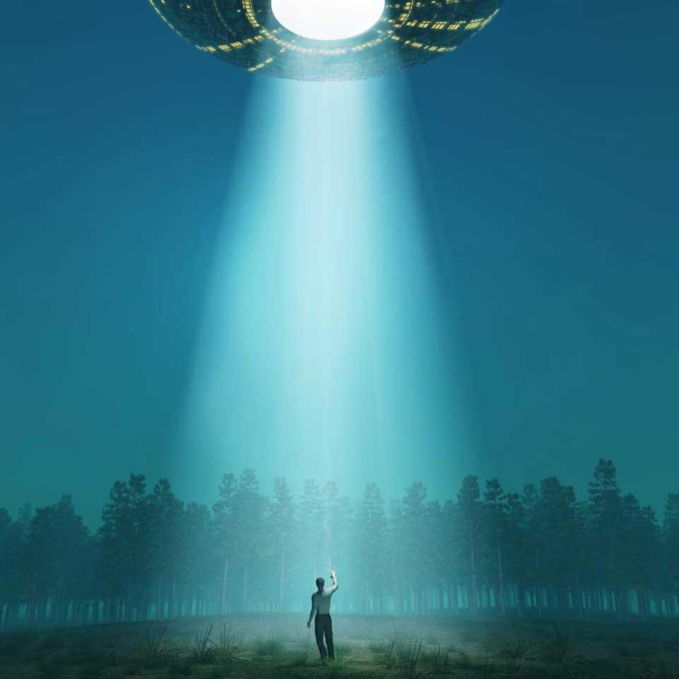 A person stands in a clearing in the cone of light of a UFO flying overhead.