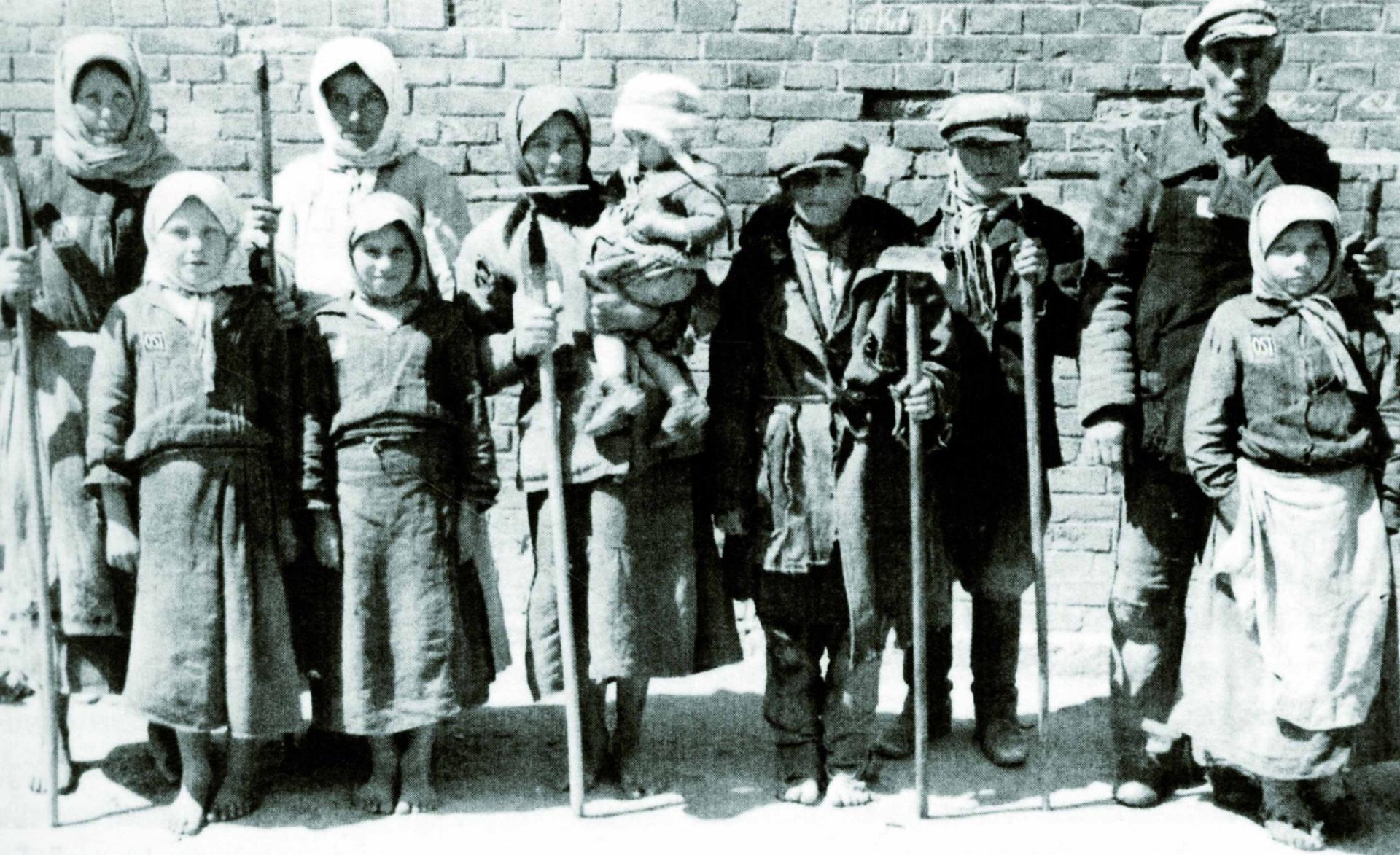 Ten people, mostly unshod and mostly children, with farming implements