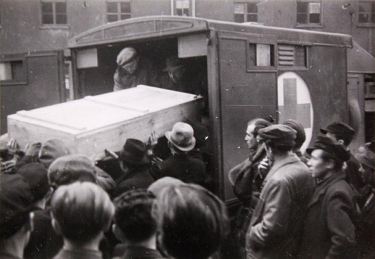 The body of Shmuel Dancyger is lifted into a van in a wooden box by several people.