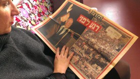 A woman is reading a hebrew newspaper with pictures of Rabin and the peace rally.