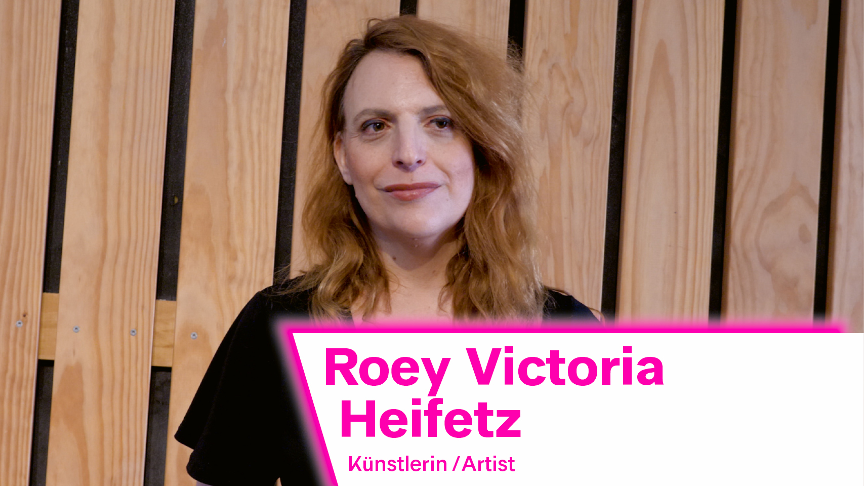 Das Interview zeigt die israelische Künstlerin Roey Victoria Heifetz. Sie trägt ein schwarzes Kleid und hat rotblonde Haare.