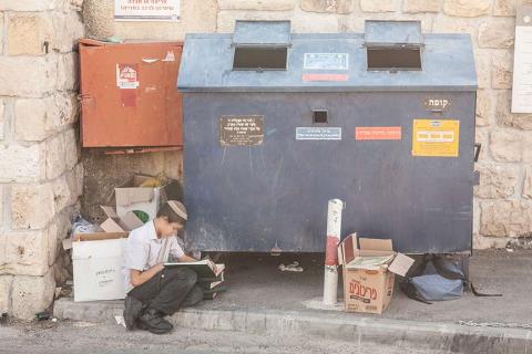 A boy sits reading in front of a container on the side of the road.