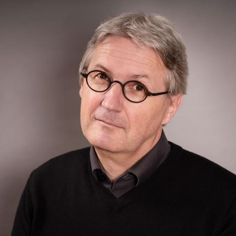 A man with small black glasses and short gray hair looks friendly into the camera.