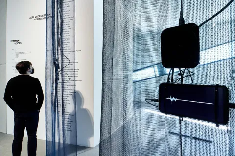 Room view of the exhibition with visitor, in the foreground a screen with a voice wave