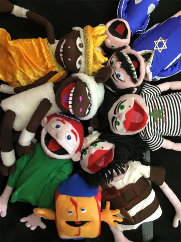 Acht bunte Klappmaulpuppen liegen mit den Köpfen zueinander im Kreis und lachen die Betrachtenden an.