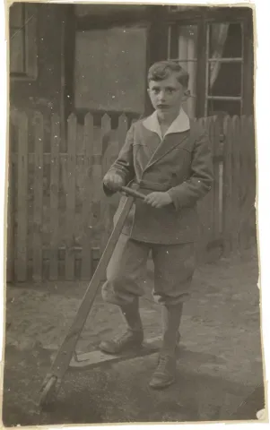 Walter Frankenstein’s photograph as a child in fine clothing and standing in front of a fence with a scooter.