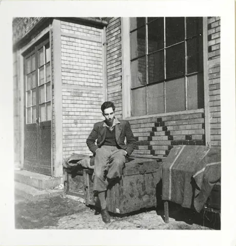 A young man sits in front of a house (black and white photo).