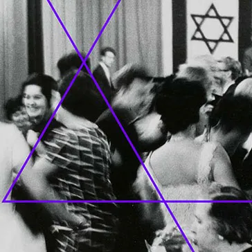 Black and white photograph: people dressed in festive outfits dancing; in the background is a stage decorated with two Israeli flags and a band playing.