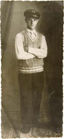 Portrait of a standing young man in a sailor's cap and a hand-knit sweater. He has a friendly look on his face and a delicate build.