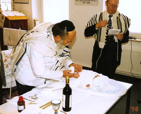 Elderly man circumcising a baby laying on a table