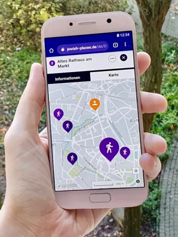 One hand holds a smartphone on which a map with colorful place markers is open.