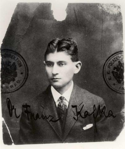 Schwarz-weißes Passbild eines jungen Mannes mit gegeeltem Mittelscheitel, auf dem Foto sind Stempel und die Unterschrift: Dr. Franz Kafka.