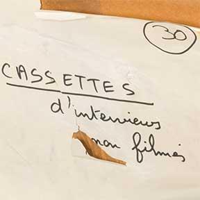 Teils beschädigter Zettel mit der handschriftlichen französischen Beschriftung „Cassettes d’interviews [de mon?] filmes“ (Kassetten mit Interviews [meines?] Films)