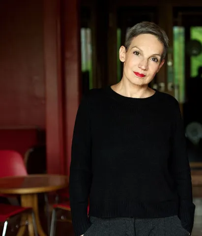 Portrait of Marion Brasch, hands in pockets, with bar table in the background