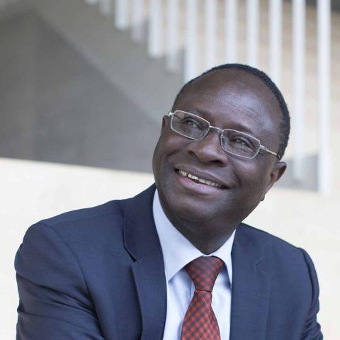 Karamba Diaby is sitting on a staircase, wearing a blue suit with a red check tie.