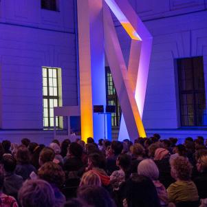 The glass courtyard is filled with people and illuminated in purple.