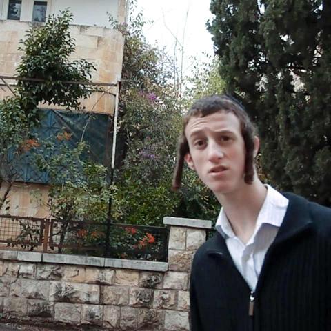 In einem jerusalemer Wohnviertel schaut ein junger Mann mit Schläfenlocken mit neugierig-überraschtem Blick in die Kamera.