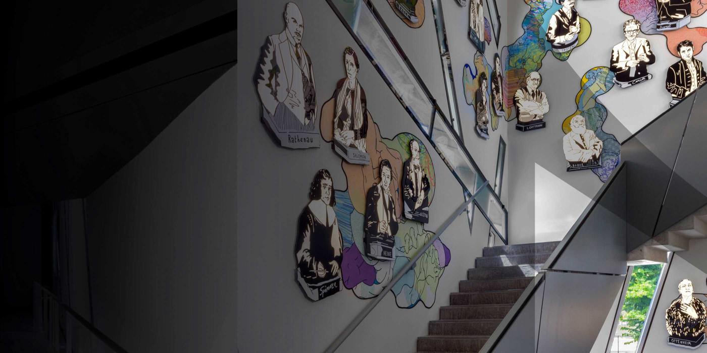 Black staircase. On the wall colorful portraits. The picture is with a gray veil that suggests the JMB logo.