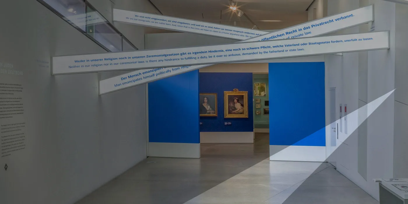 Leuchtschrift mit dem französischen Begriff égalité, Leuchtschilder mit Text, im Hintergrund Gemälde. Das Bild ist mit einem grauen Schleier der das JMB-Logo andeutet.